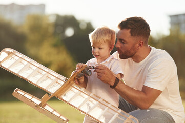 Teaching the kid how to fix it. Father and son are on the field together with toy plane