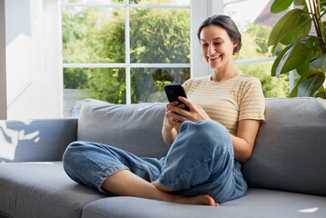 Obraz premium Woman with mobile phone sitting on sofa at home