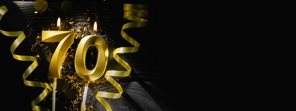 Golden candles number seventy burning brightly, celebrating 70th birthday anniversary. Festive ribbons and confetti on black background, creating elegant celebratory banner.