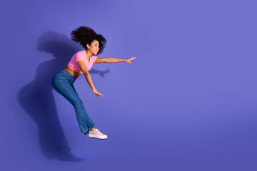 Young happy woman in casual outfit jumping and gesturing energetically against a purple background, expressing excitement and freedom