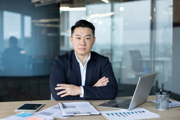 Portrait of a serious young Asian male businessman, director and owner sitting at a desk in the office, looking confidently at the camera
