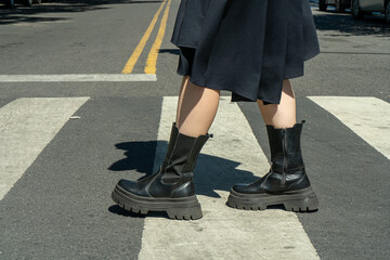 Fototapeta premium Woman wearing black boots crossing the street on pedestrian crossing