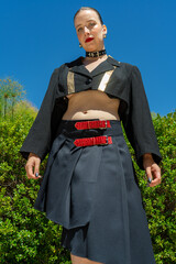 Fashion model posing in a garden wearing a black and gold cropped jacket and skirt
