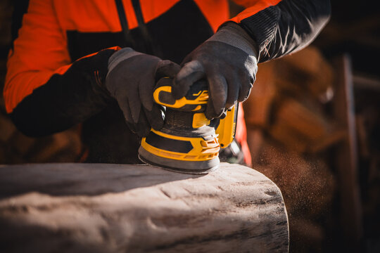 Man hand grinding with cordless wood grinder. Woodwork with aku grinder. Close up of grinder. Man dressed in reflective workwear. Close up of sanding a wood with orbital sander at workshop.