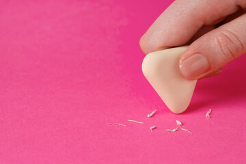 Woman using eraser on pink background, closeup. Space for text
