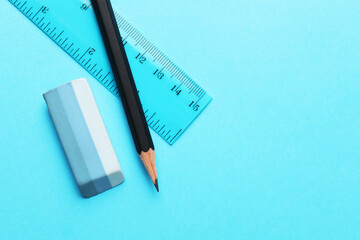 Eraser, pencil and ruler on light blue background, top view. Space for text