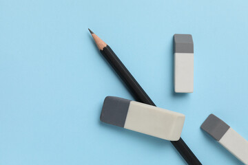 Erasers and pencil on light blue background, top view. Space for text