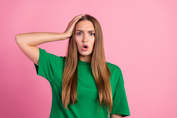 Young woman expressing surprise with hand on head against pink background, showcasing stylish...