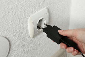 Woman plugging USB power adapter with charge cable into electrical socket indoors, closeup
