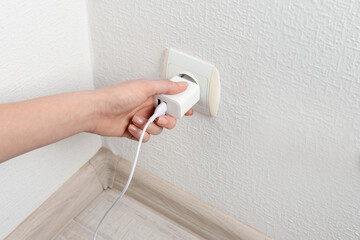 Woman plugging USB power adapter with charge cable into electrical socket indoors, closeup