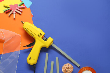 Hot glue gun and handicraft materials on blue background, flat lay. Space for text
