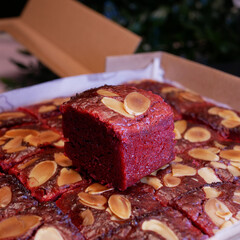 Dark red brownie pieces in a tempting paper box with crunchy almond topping on top. A sweet and delicious snack to boost spirits and happiness throughout the day.