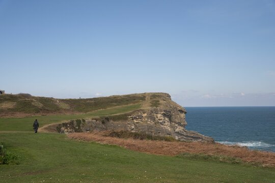 Scenic coastal landscape with a solitary figure walking along a grassy cliff