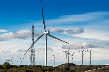 Wind turbines spinning in a renewable energy farm, with electrical towers in the background, highlighting energy infrastructure.