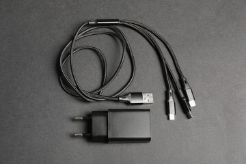USB power adapter and triple charge cable on black background, flat lay