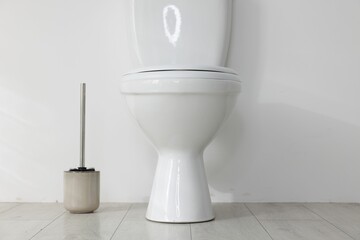 Toilet and brush on floor near white wall