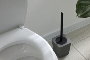 Toilet and brush near white wall in bathroom