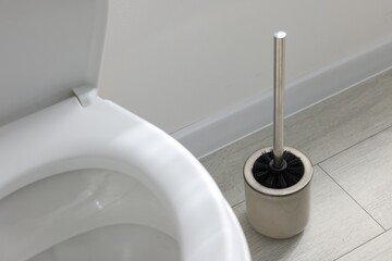 Toilet brush with metal handle and bowl on floor indoors