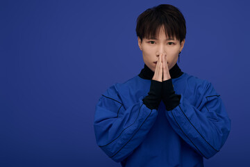 Young Asian man expresses gratitude against a vibrant blue backdrop during a creative session