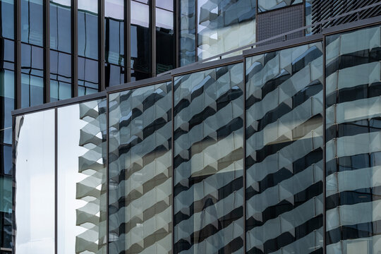 Mirrored glass facade of a high-rise reflecting an adjacent tower, forming a layered architectural perspective.