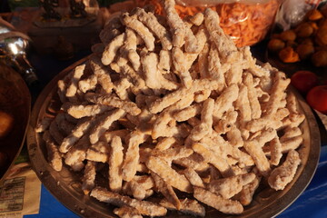 A large pile of Lakdi Mithai, an Indian sweet snack, in a metal bowl, also known as Lakri Mithai or Goja, is a crispy, crunchy sweet made from flour, ghee, and sugar