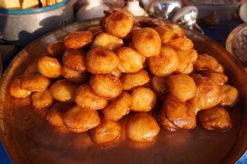 Balushahi, a traditional Indian sweet, on a large, round, possibly copper or brass plate which is a flaky, doughnut-like pastry that is deep-fried and then soaked in sugar syrup