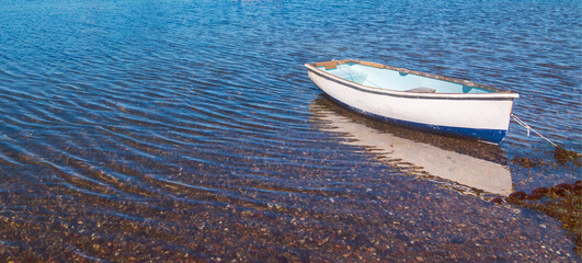 Rowing Boat anchored at sea shore with a reflection of the boat in the shingle of the water.
