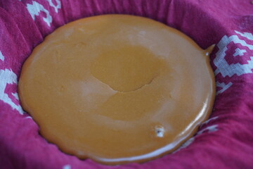 A flat disc of caramelized jaggery resting on a pink and white patterned cloth
