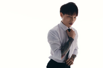 Handsome young Asian man adjusting tie with tattooed arm against a minimalist backdrop