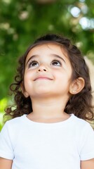 Young girl gazes up in wonder under lush greenery during a warm sunny day in the park