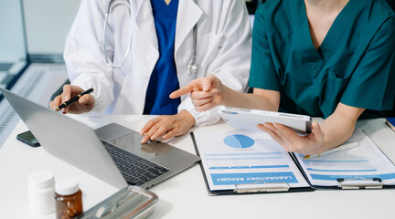 Medical team having a meeting with doctors in white lab coats and surgical scrubs seated at a table