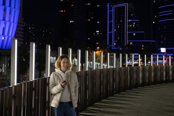 Woman Using phone in Modern City at Night, typing messages, using smart applications, and embracing the urban lifestyle.
