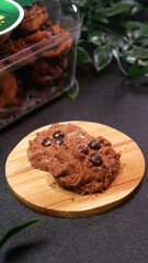 Clear plastic jars containing chocolate cookies with green stickers typical of Eid al-Fitr, several cookies on wooden stands, with artificial leaf decorations creating a festive Eid atmosphere.