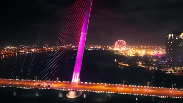 Tran thi ly bridge glowing pink, spanning da nang's nocturnal skyline, featuring dramatic cable supports, illuminated cityscape, and distant ferris wheel creating vibrant nighttime scenery