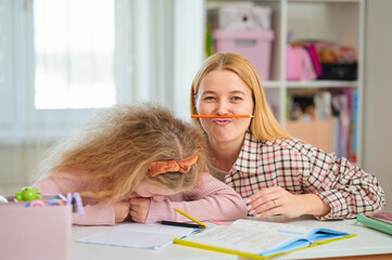Mother and daughter playfully hold pens under noses, laughing during homework time. Fun study...