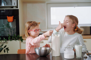 Flour-covered girls giggle while smearing powdery faces, hands transforming cheeks and noses into...