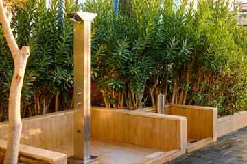 Modern outdoor stainless steel shower against lush green plants. Natural wood and metal...