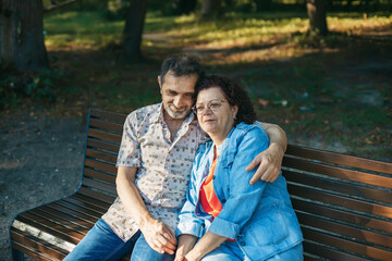 Elderly couple hugging while sitting on a bench in the park, symbolizing lasting love, trust, and...