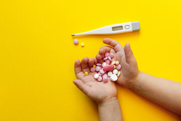 pharmacy colorful medicament pills on child (toddler) hands and thermometer on yellow background