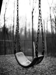 Empty swing in deserted park during winter amid bare trees