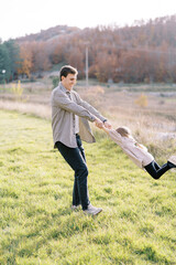 Smiling dad twists little girl by the hands on a sunny autumn meadow