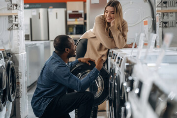 Sitting and opening. Man and woman are choosing washing machine in the store