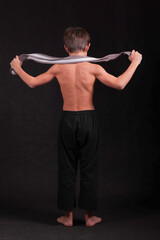 athletic boy with muscular back with martial arts belt draped between his arms in kimono pants