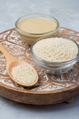 Raw sesame seeds and sesame paste in bowls on wooden stand.