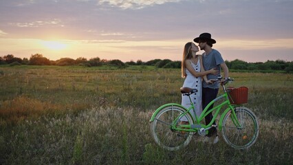 Obraz premium A couple sharing an affectionate embrace at sunset while riding a bicycle through a scenic field