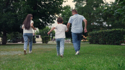 Obraz premium happy family, boy laughing holding father mother by hand, child father mother running in summer park, family trip, child play, family run, boy son running with parents park, group people running feet