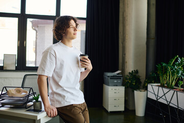 Young man enjoying coffee while contemplating work in a stylish office environment
