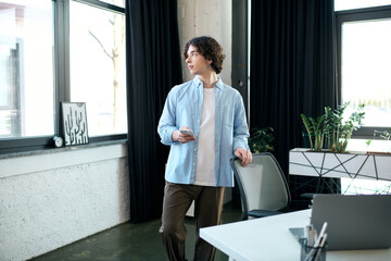 Young man in a modern office looking thoughtful while holding a smartphone during work hours