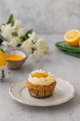 Lemon Poppy Seed Cupcakes with lemon curd and cream cheese topping. Cupcake in form of Fried Egg. Colourful Easter eggs, flowers on a stone background. Spring concept. Easter holiday and festive food.