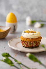 Lemon Poppy Seed Cupcakes with lemon curd and cream cheese topping. Cupcake in form of Fried Egg. Colourful Easter eggs, flowers on a stone background. Spring concept. Easter holiday and festive food.